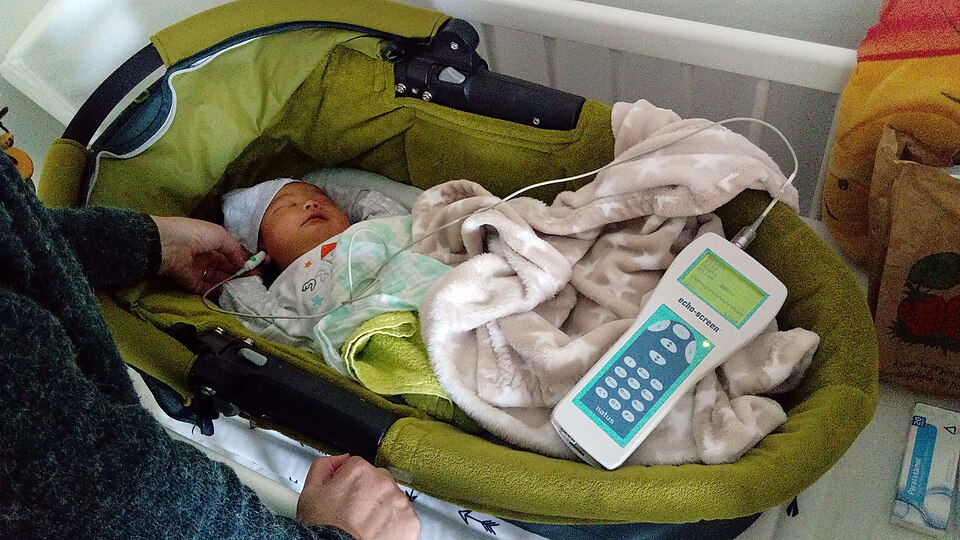 Newborn hearing screening with a probe in the ear and a tablet displaying the result